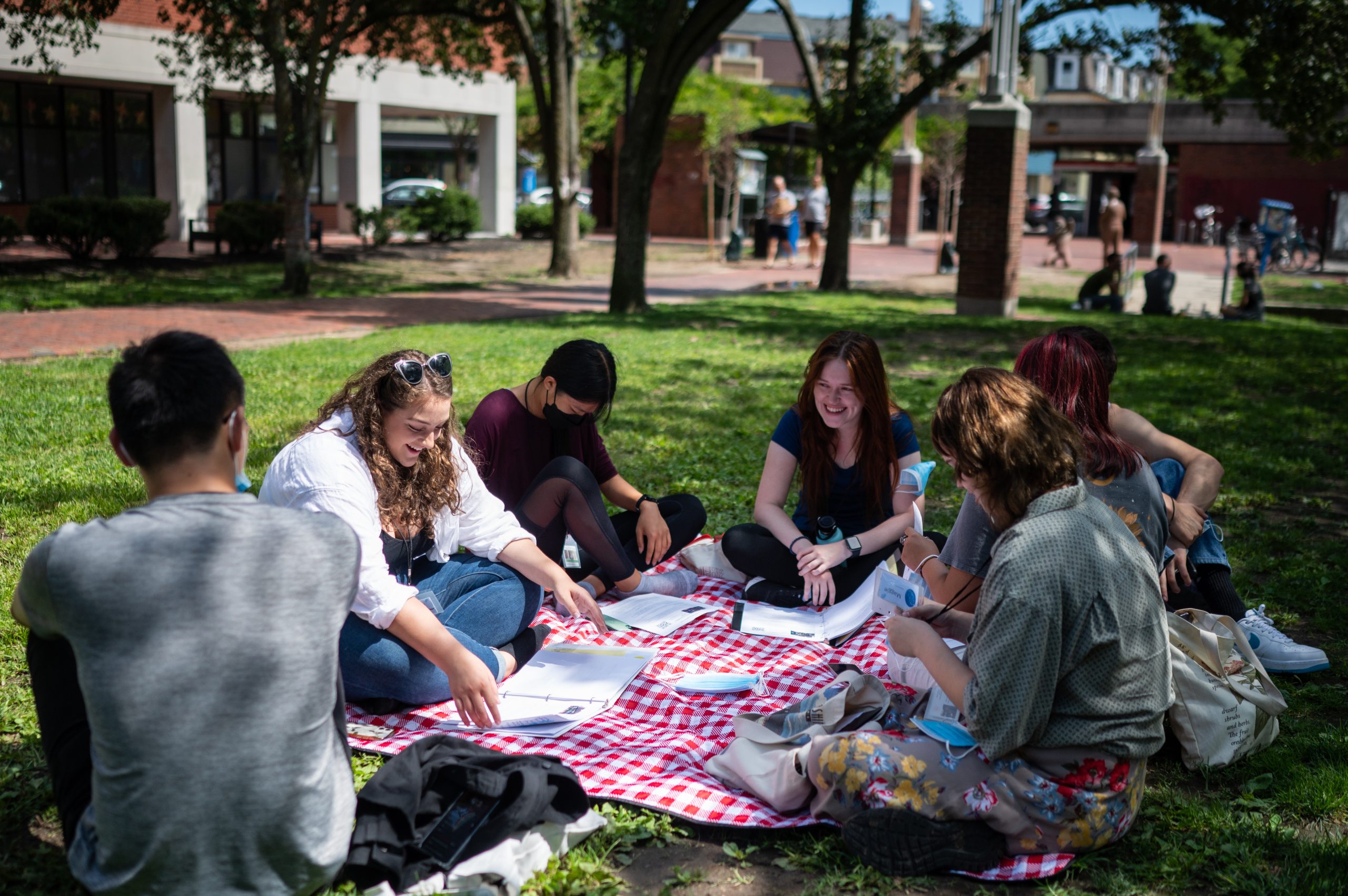 six students sitting on a picnic blanket,  they are talking