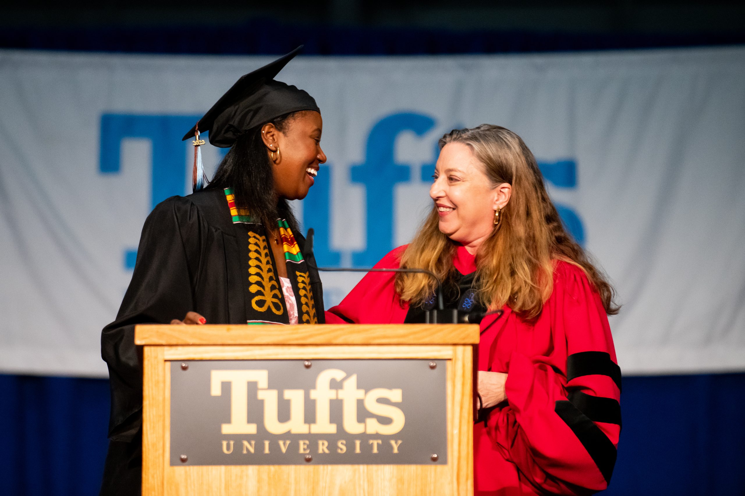 Two people smiling at each other on stage in academic regalia
