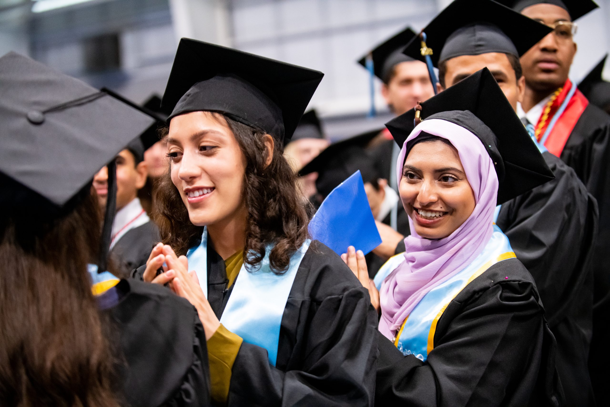 Two students in cap and gowns clapping 