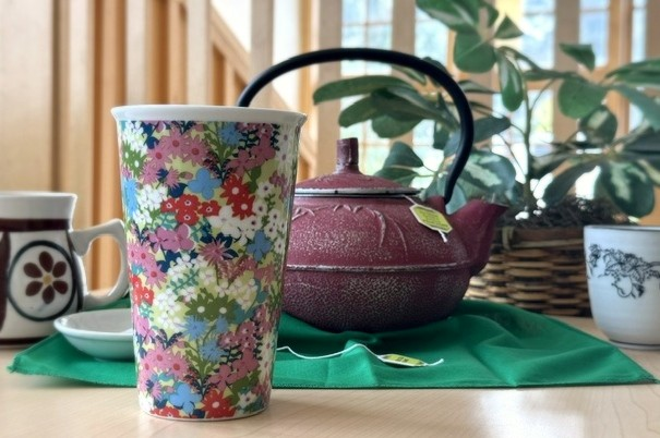 Colorful mug in the foreground, tea kettle and plant in the background